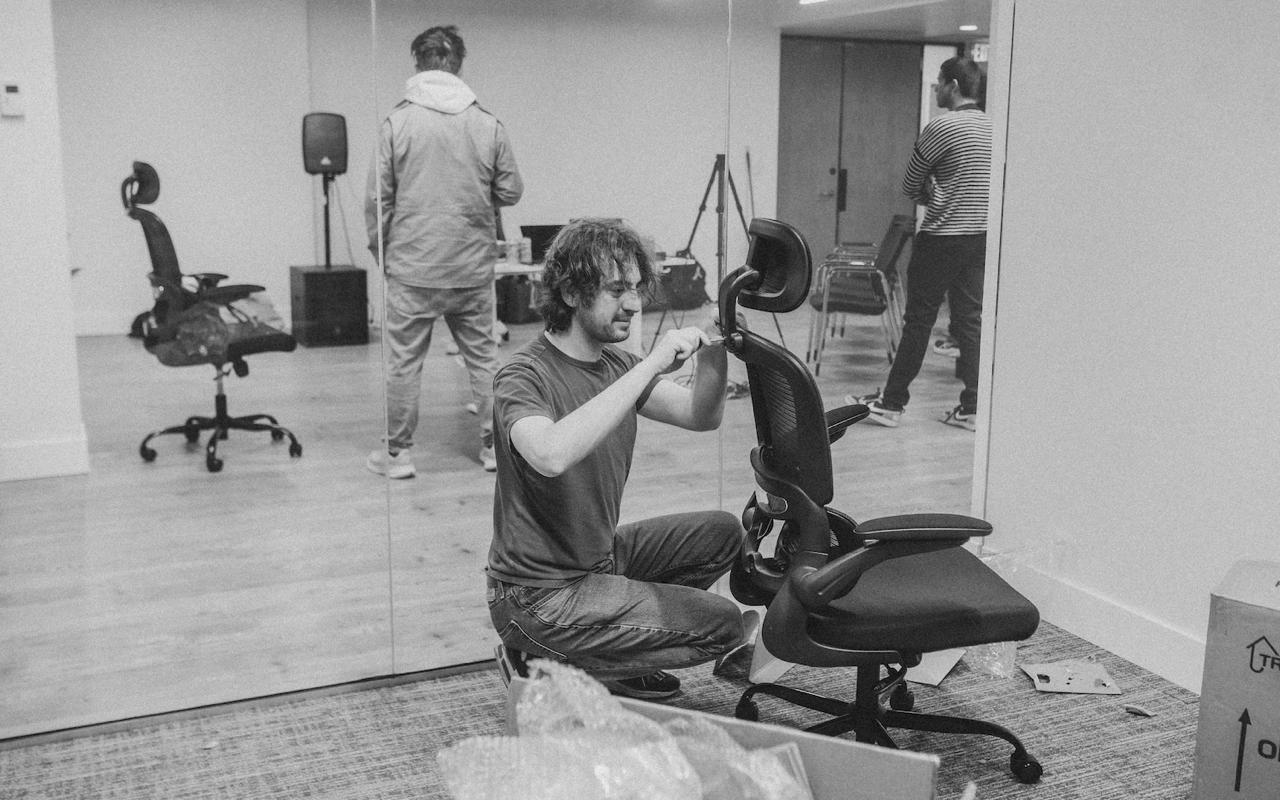 Member assembling equipment in the loft space with others setting up audio gear in the background
