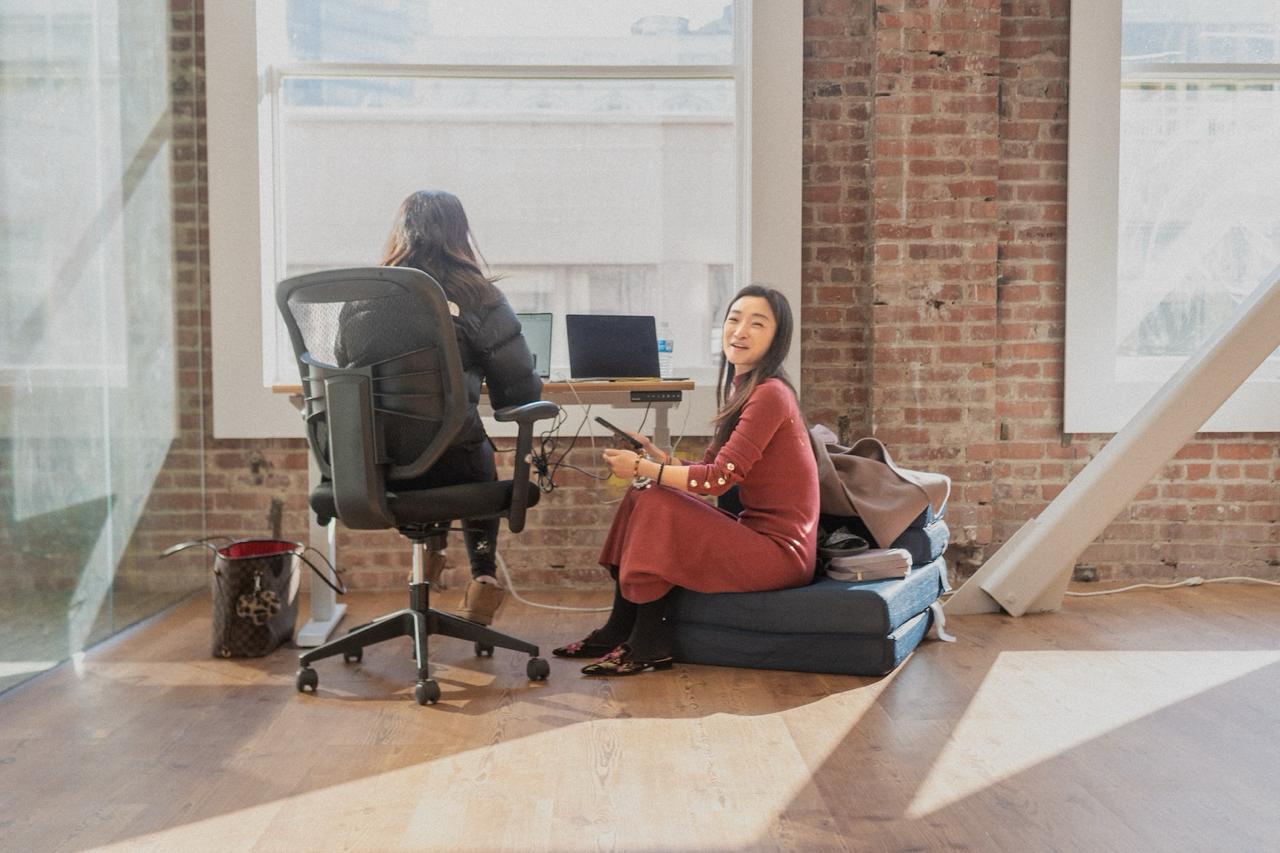 Two people hanging out in a bright loft space with exposed brick, large windows, and natural light